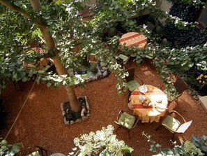 Un área de estar al aire libre con una mesa y sillas, rodeada de plantas y un árbol.