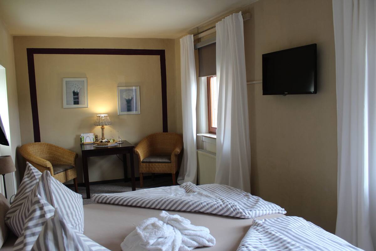 A hotel room with a bed, two chairs, a table with a lamp, and a TV on the wall.