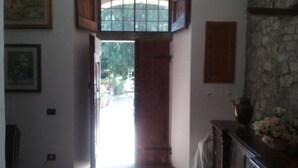 A hallway with a wooden door leading outside, a stone wall, and a vase with flowers on a wooden table. - Latera B&B (Barberino di Mugello)