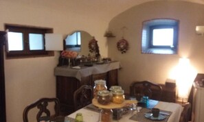 A dining area with a table set for two, featuring a candle, a glass, and a plate. There are two chairs, a window with a view, and a wall-mounted lamp. - Latera B&B (Barberino di Mugello)