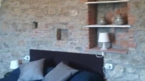A bedroom with a stone wall, a bed with pillows, and a shelf with kitchen items. - Latera B&B (Barberino di Mugello)