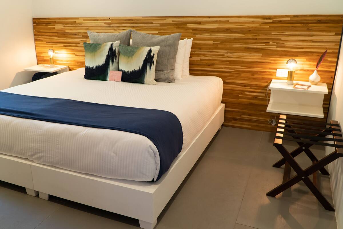 Quarto moderno com cama grande, cabeceira de madeira e mesas de cabeceira com luminárias.