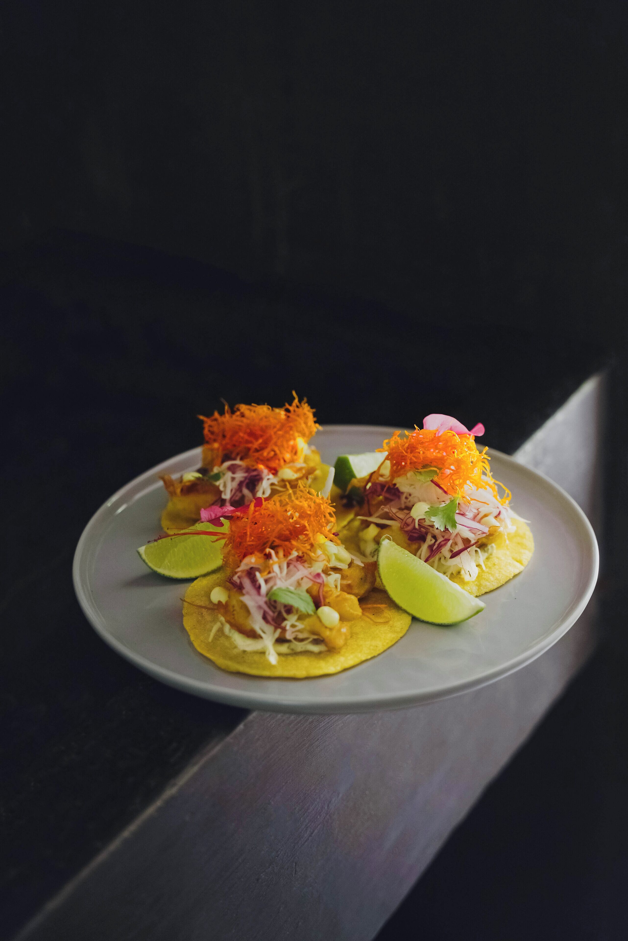 Prato de tacos com cenoura ralada e gomos de limão.