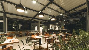 A restaurant with multiple tables and chairs, a bar area, and large windows allowing natural light. - Nya Hotel (Cóbano)