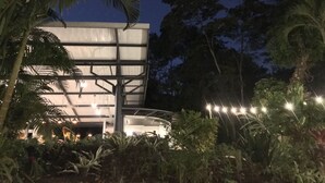 A modern building with a flat roof and large windows, surrounded by lush greenery and palm trees. - Nya Hotel (Cóbano)