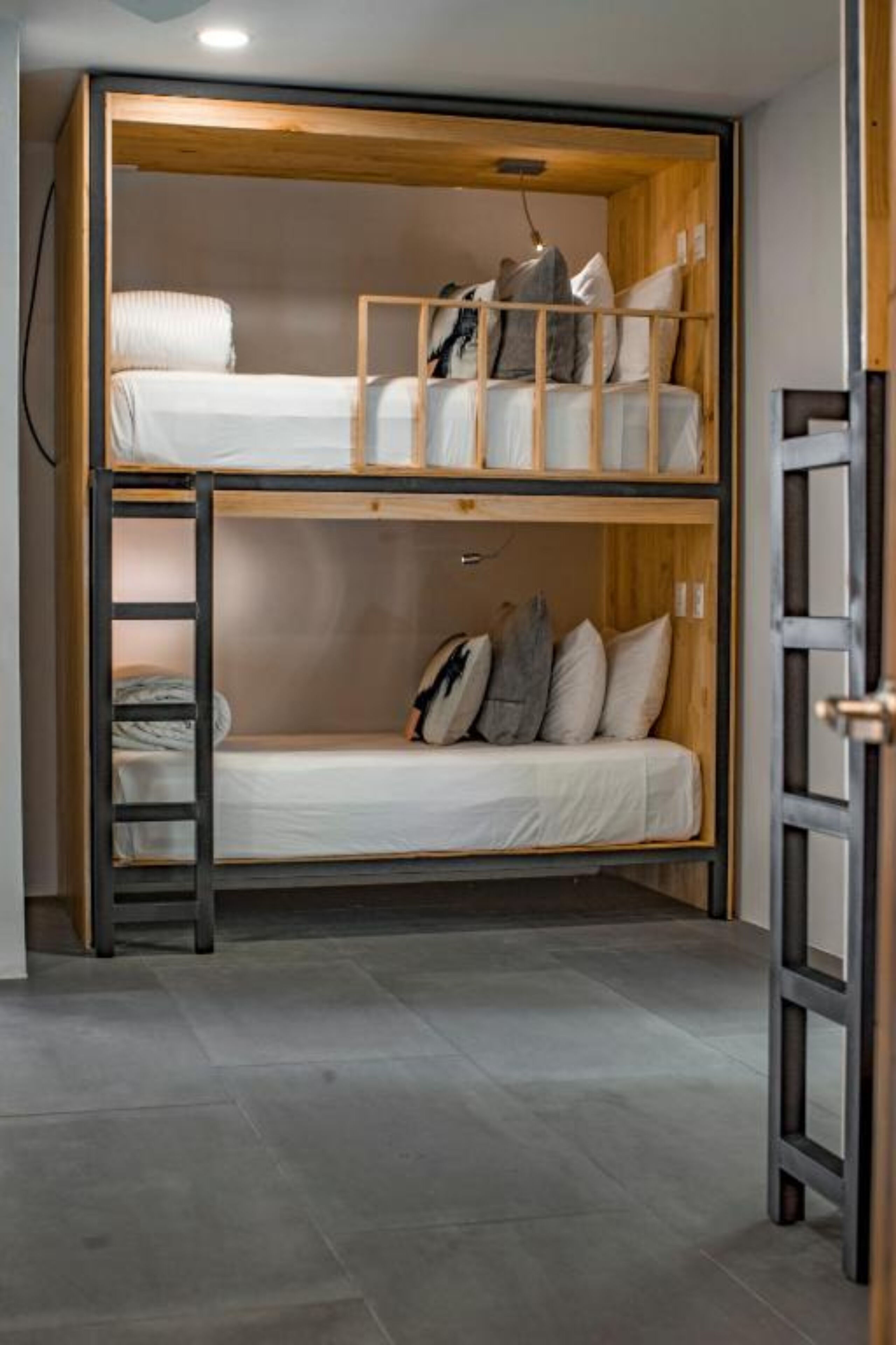 Habitación con literas de madera, una escalera y un pequeño estante.