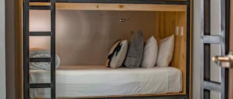 Habitación con literas de madera, una escalera y un pequeño estante.