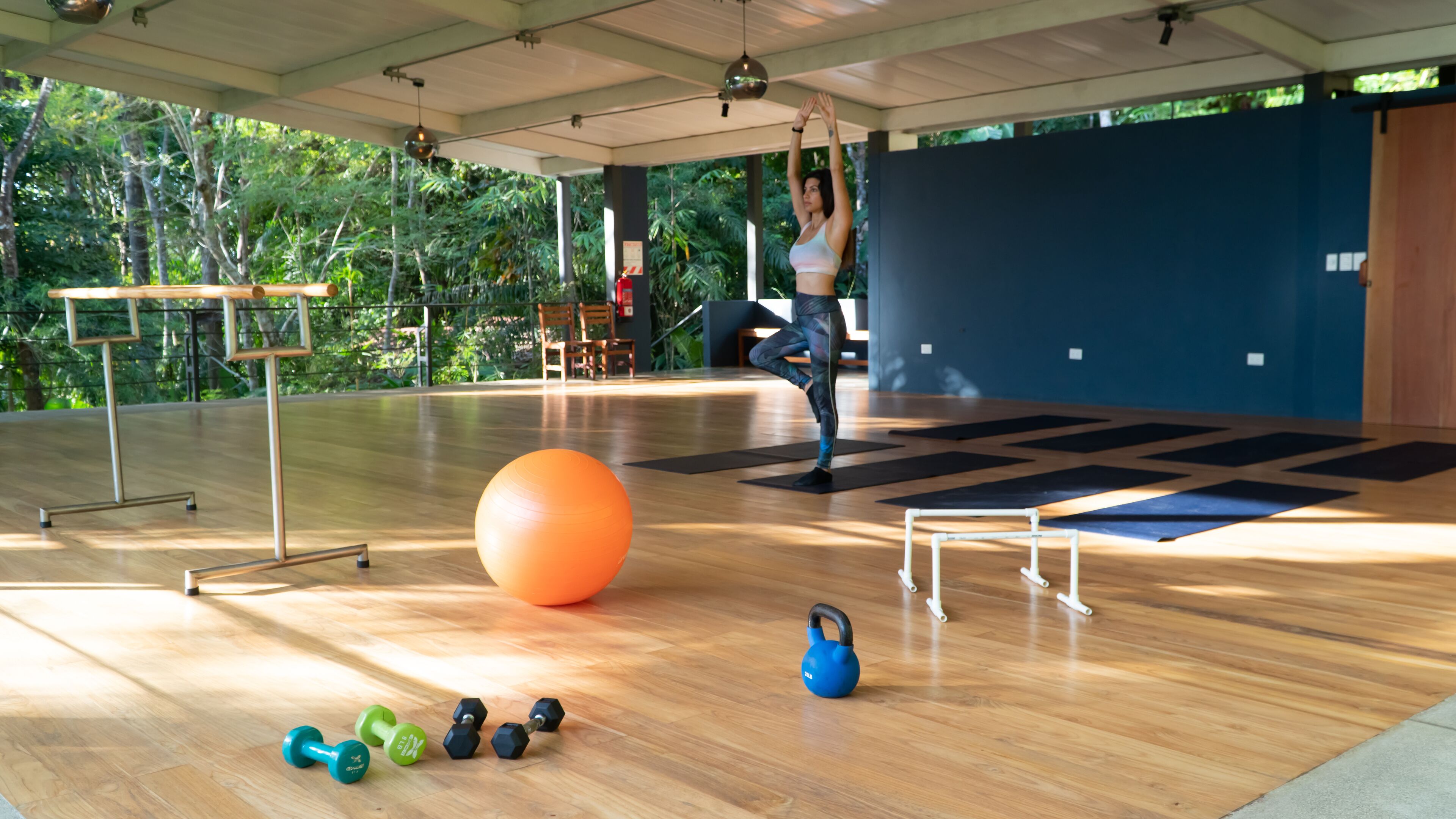 A spacious indoor gym with wooden flooring, exercise equipment, and a large orange exercise ball.