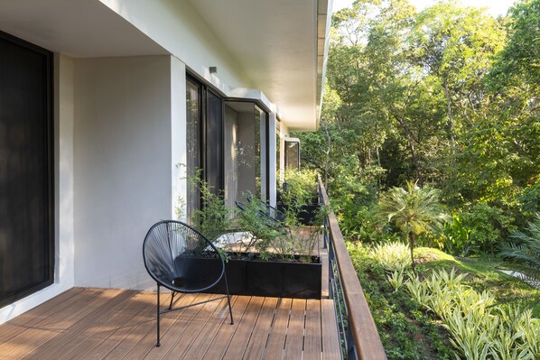 A balcony with a wooden floor, a black chair, and a planter with plants.
