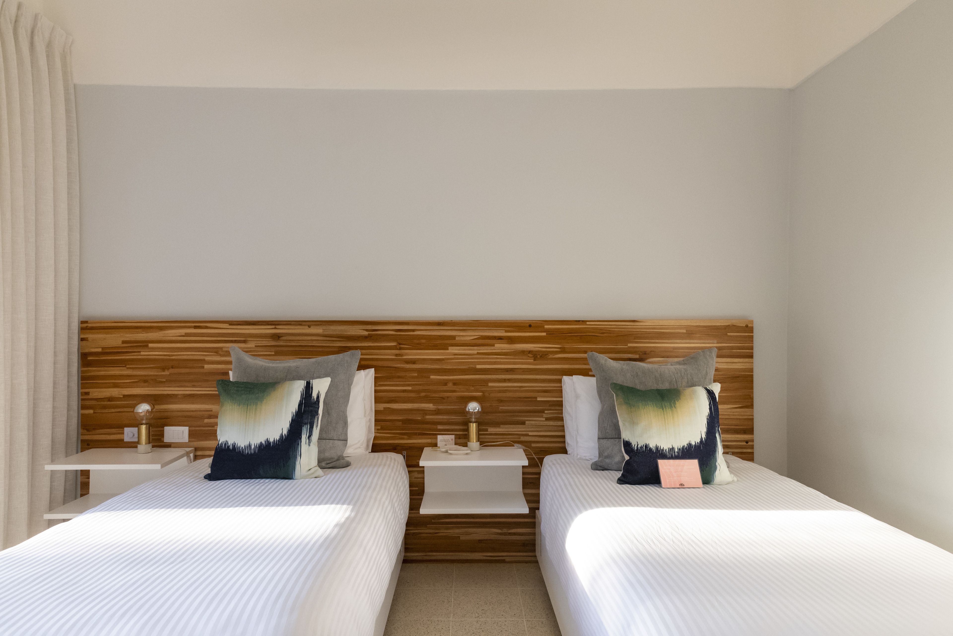 Une chambre d’hôtel avec deux lits, une tête de lit en bois, des tables de chevet et des coussins décoratifs.
