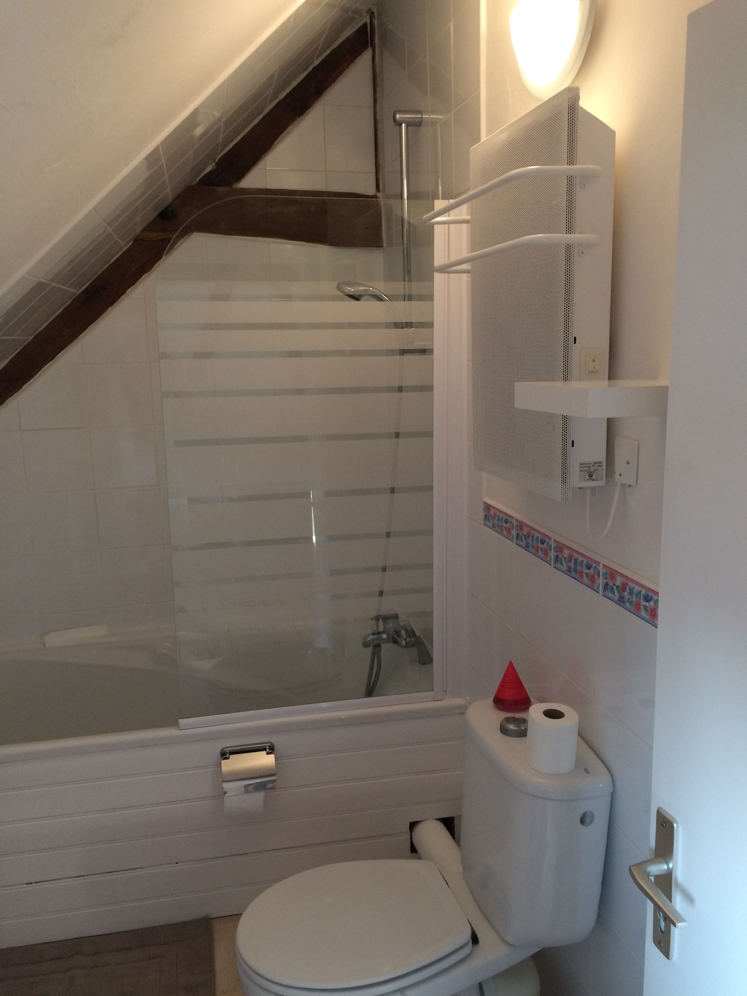 Een moderne badkamer met een douchecabine van glas, een toilet en een klein plankje met toiletartikelen.