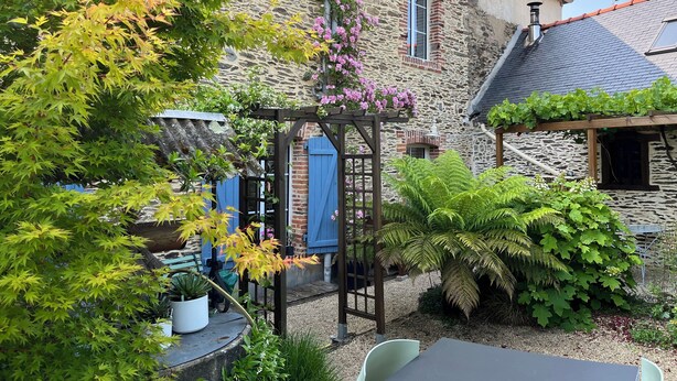 A stone building with a thatched roof patio, a wooden pergola, and a variety of plants.
