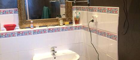 Un baño con lavamanos pedestal, un espejo con marco dorado y un mueble de tocador de madera.