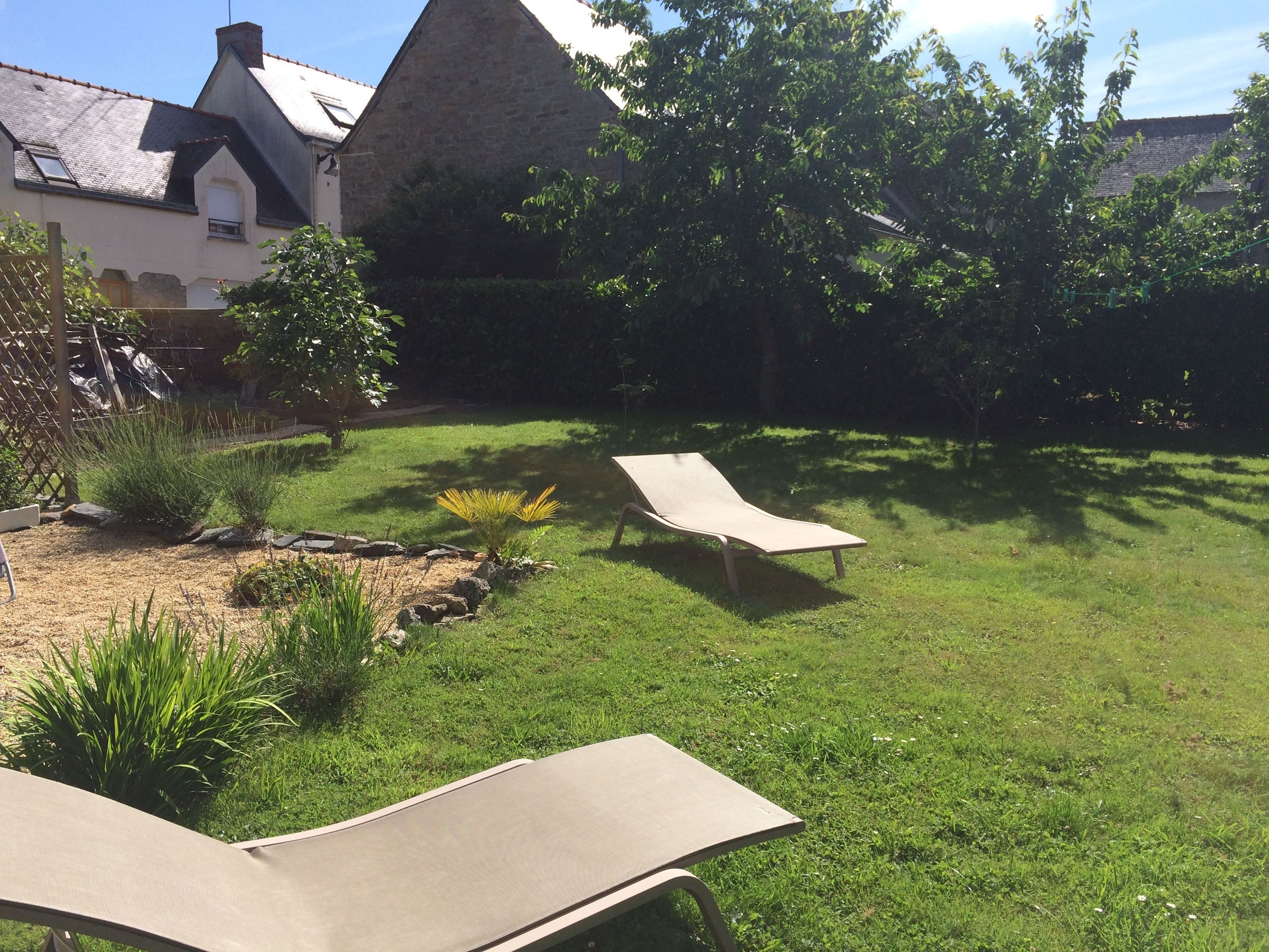 Un jardin avec deux chaises longues, un bâtiment en pierre et une variété de plantes.