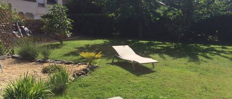 Un jardin avec deux chaises longues, un bâtiment en pierre et une variété de plantes.