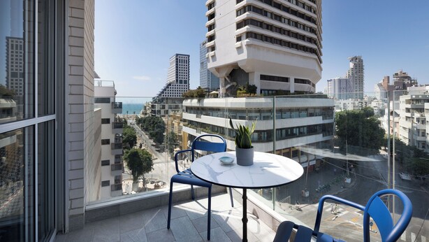 A balcony with a round table, two chairs, and a potted plant. - Bauhaus Boutique by TLV2rent (Tel Aviv)