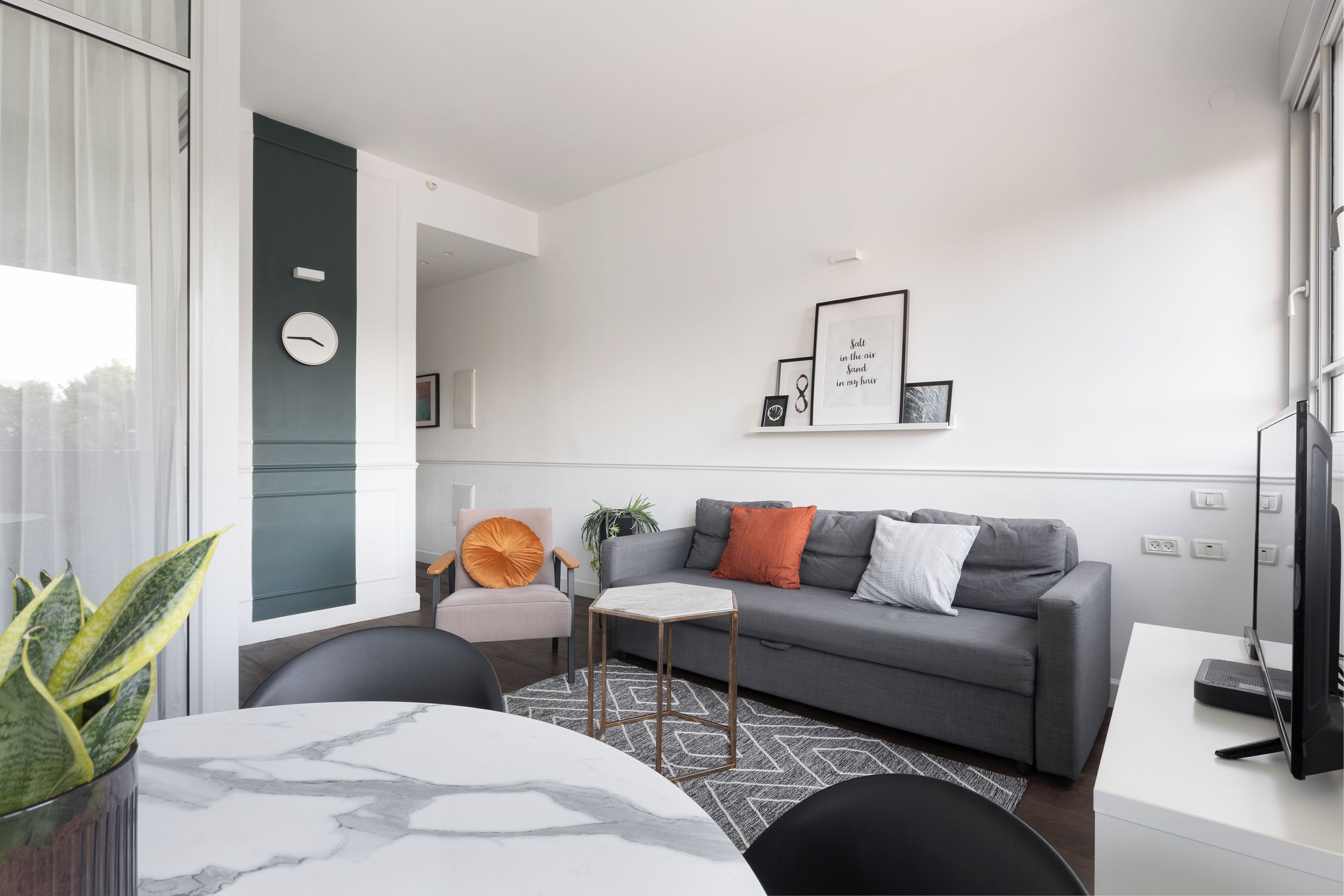 Un salon moderne avec un canapé gris, une petite table d’appoint, une plante en pot et une grande fenêtre.
