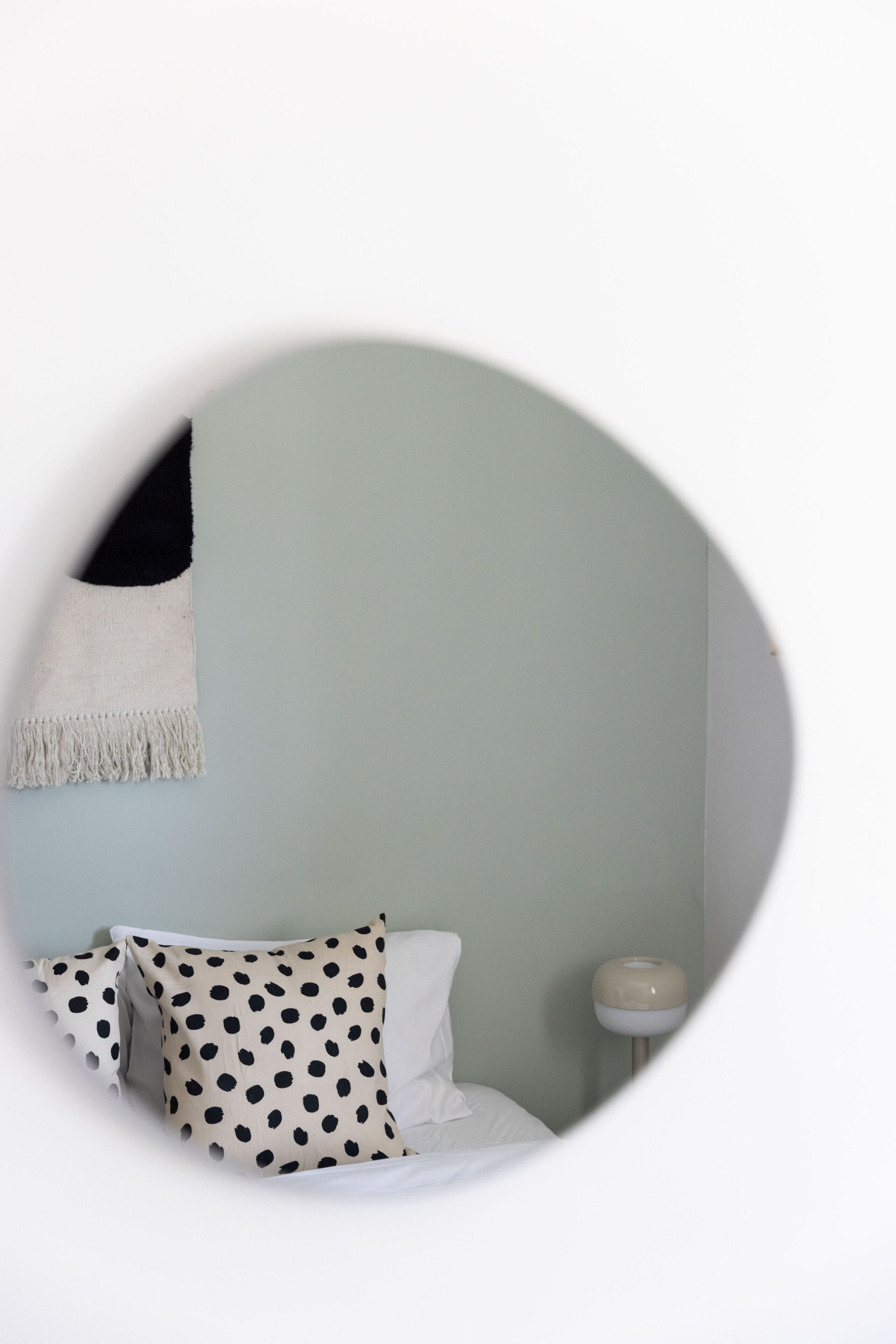 Vista circular desde una ventana de un dormitorio con cama, almohadas, lámpara de noche y toalla colgada en la pared.