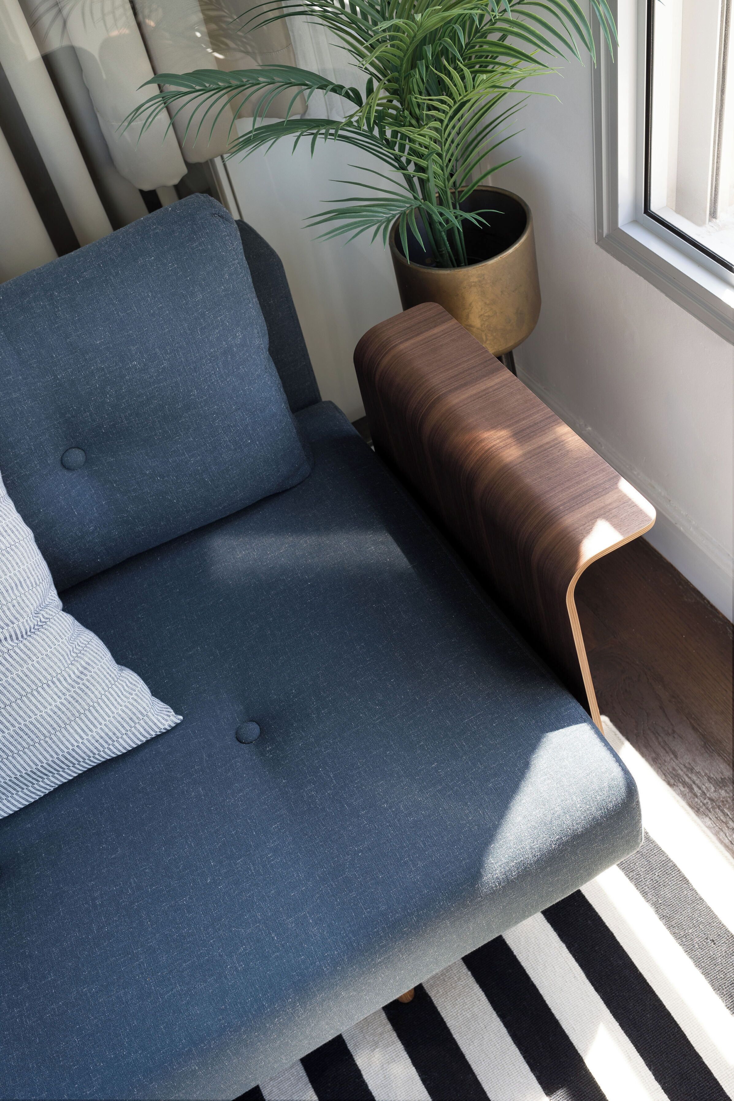 A modern living room with a blue sofa, a wooden side table, and a potted plant.