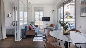 A modern living room with a sofa, a dining table, and a TV mounted on the wall. - Bauhaus Boutique by TLV2rent (Tel Aviv)