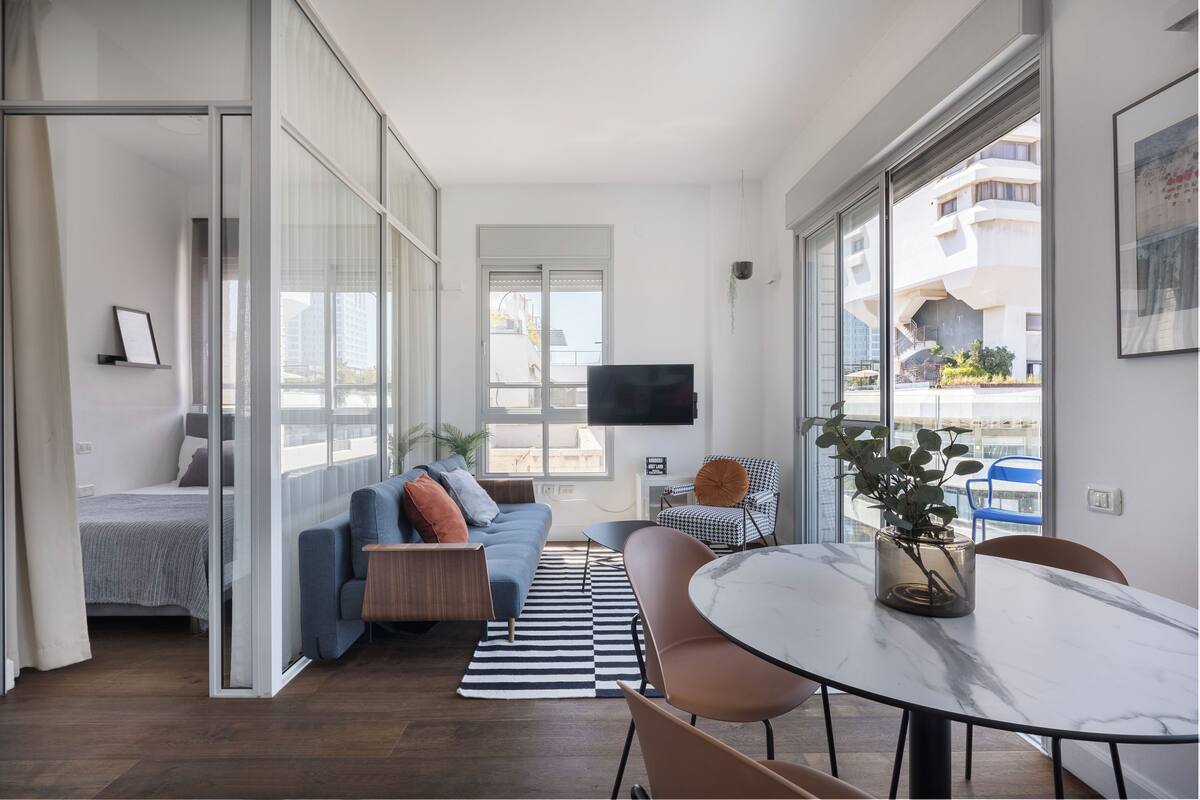 A modern living room with a sofa, a dining table, and a TV mounted on the wall.