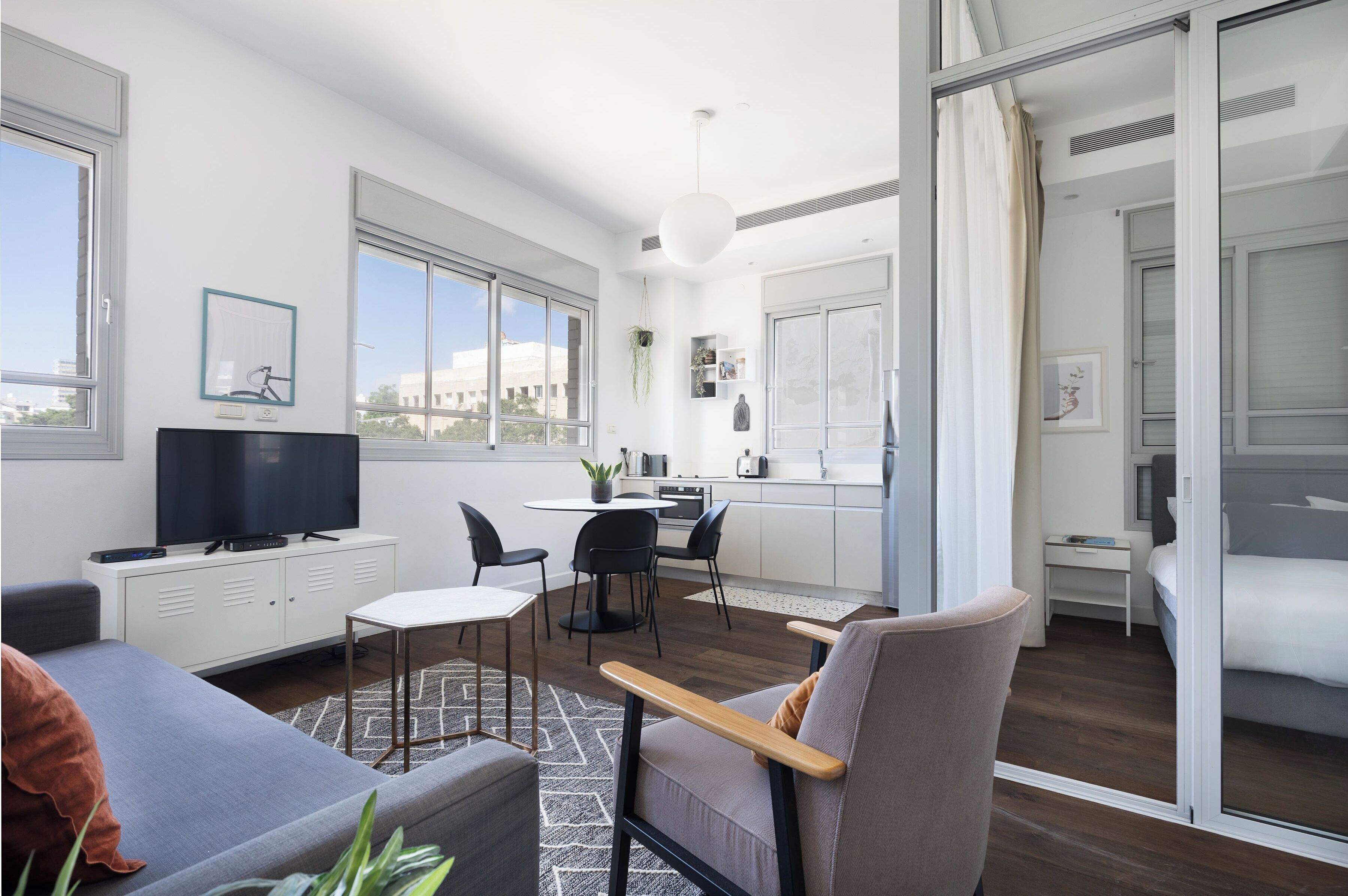 A modern hotel room with a sofa, a dining area, a TV, and a sliding door to a balcony.