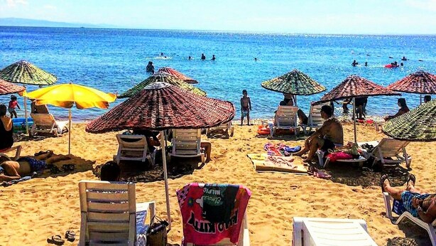 Una playa con tumbonas y sombrillas, cielo azul despejado y el océano al fondo.