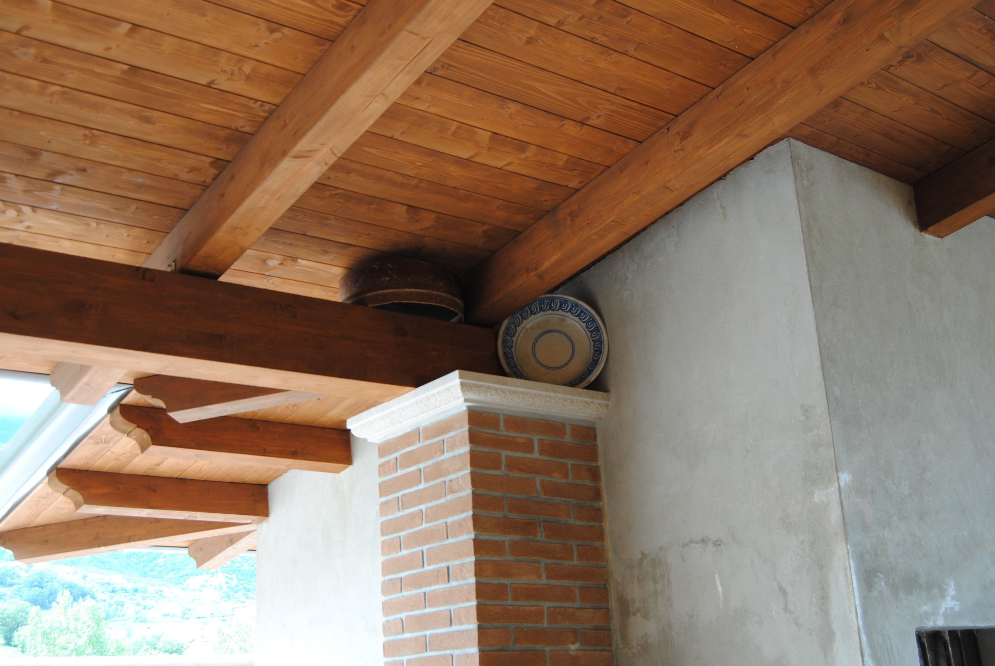 Un plafond en bois avec des poutres apparentes, une cheminée en briques et une assiette décorative accrochée au mur.