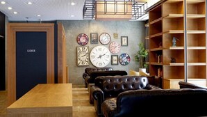 A modern interior with leather sofas, a wooden table, and a wall decorated with clocks. - Hotel Relief Sapporo Susukino (Sapporo)