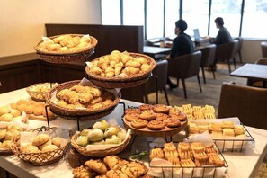 A buffet table with various baked goods, including croissants, muffins, and pastries, in a restaurant setting.