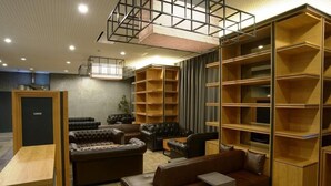 A modern interior with leather sofas, wooden shelving units, and a mezzanine level. - Hotel Relief Sapporo Susukino (Sapporo)