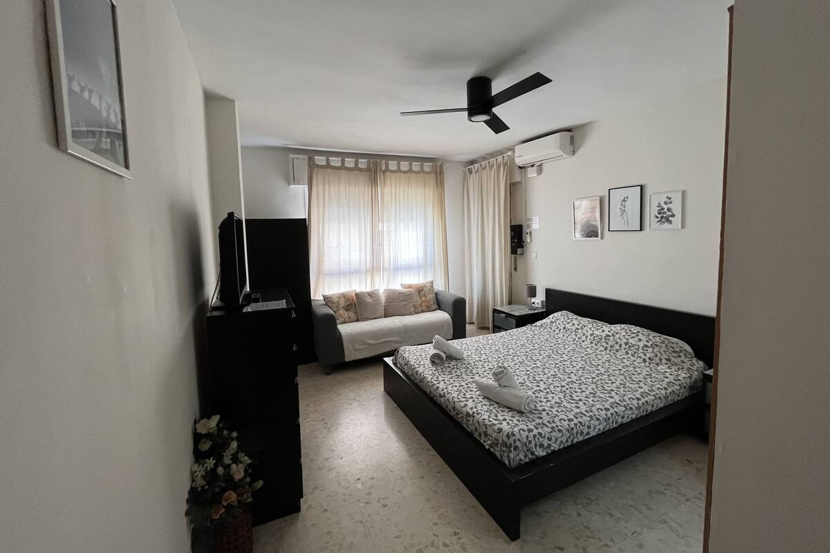 A bedroom with a bed, a TV, a desk, and a window with curtains.