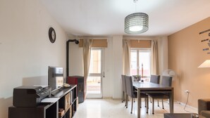 A modern living room with a dining area, a printer, a bookshelf, and a view through the window. - Rafaela Guest House (Málaga)