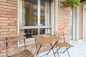 Un área de estar al aire libre con bancos de madera, una mesa, una planta colgante y un muro de ladrillo.