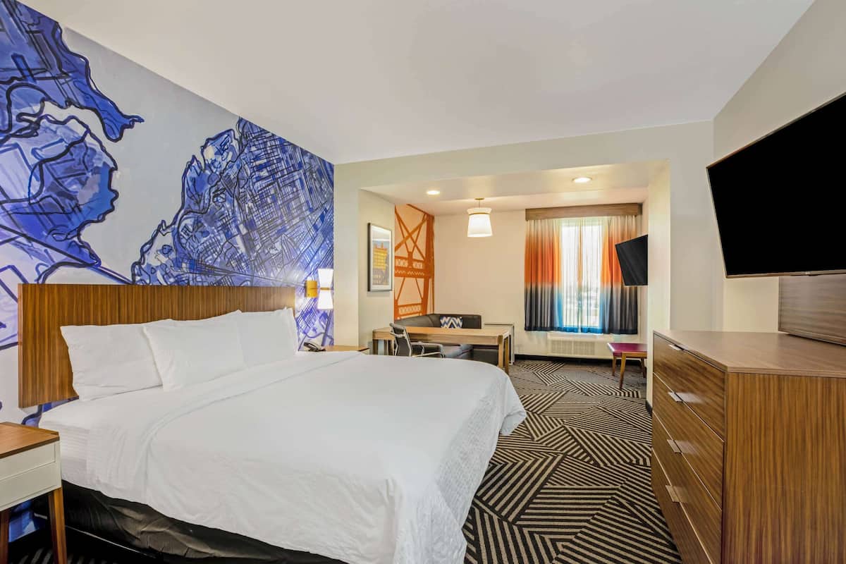 A hotel room with a large bed, a desk, a chair, a TV, and a patterned carpet.