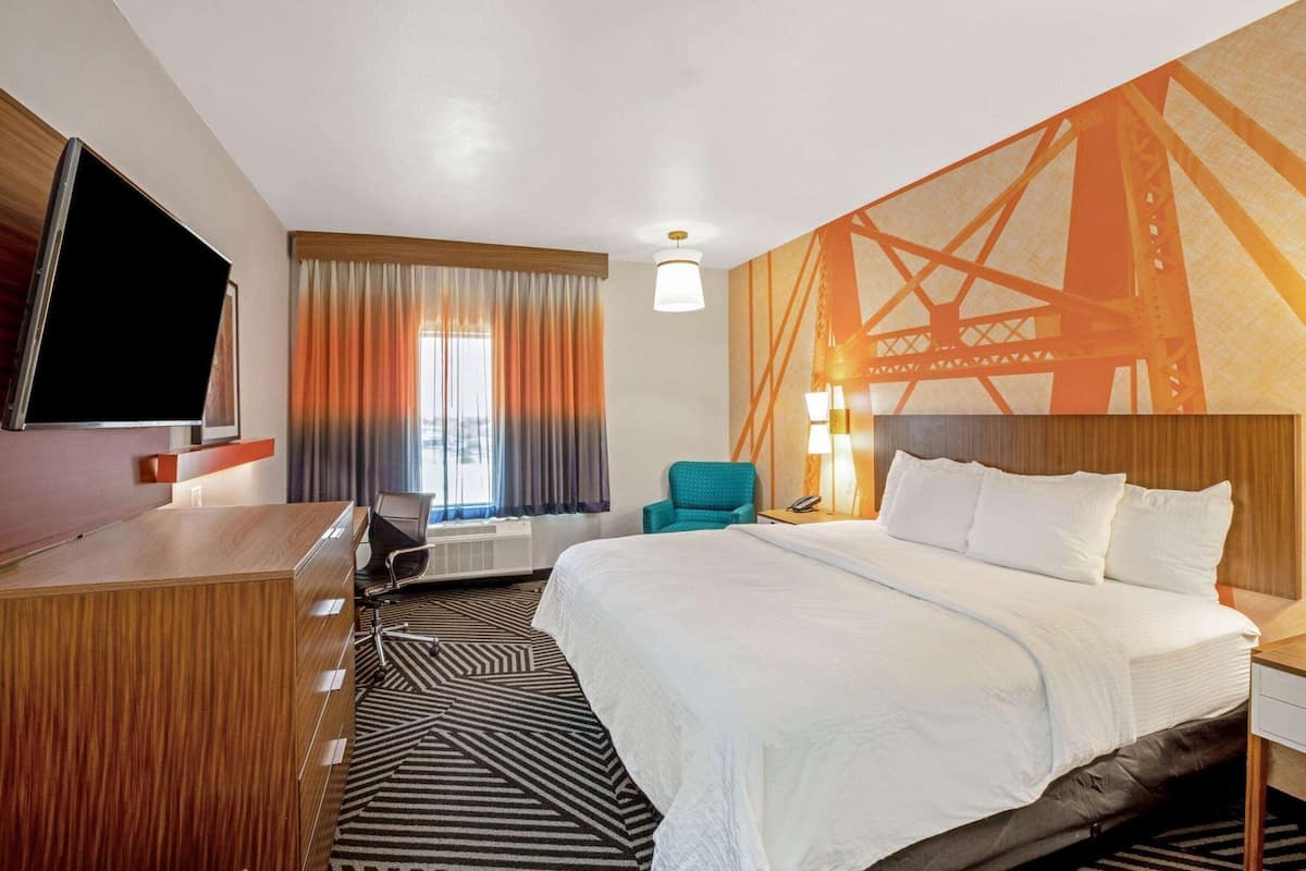 A hotel room with a bed, a desk, a chair, a TV, and a window with curtains.
