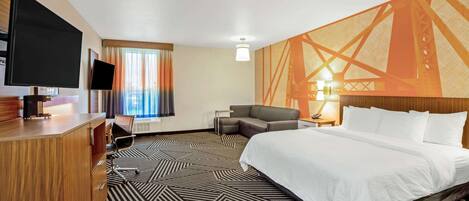 A hotel room with a large bed, a desk with a flat-screen TV, a sofa, and a patterned carpet.