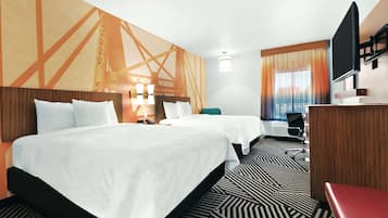 A hotel room with two beds, a desk, a TV, and a large window with curtains.