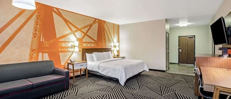 A hotel room with a bed, a desk, a chair, a sofa, a TV, and a wall mural.