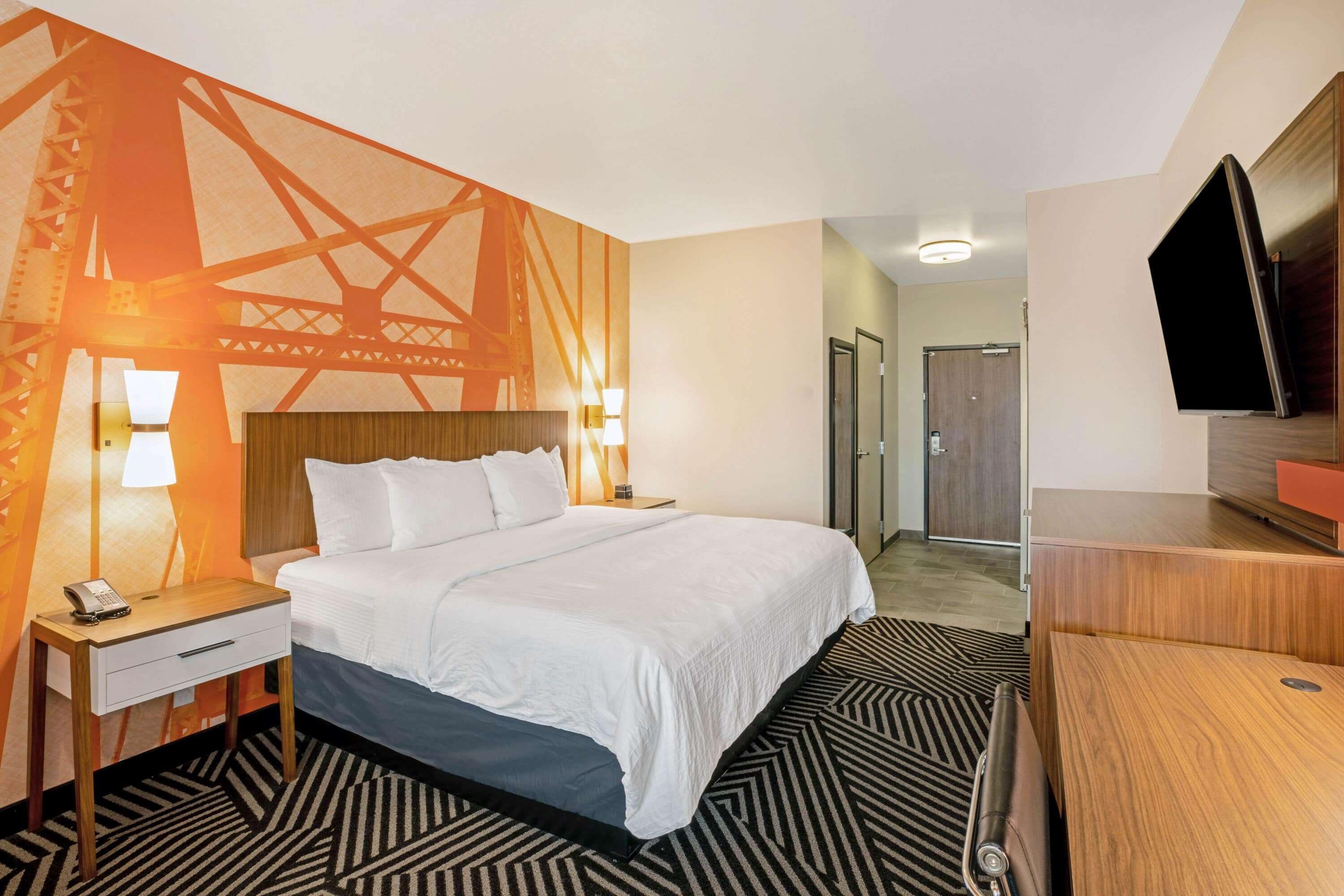 Une chambre d’hôtel avec un lit, des tables de chevet avec des lampes, une télévision et une moquette à motifs.