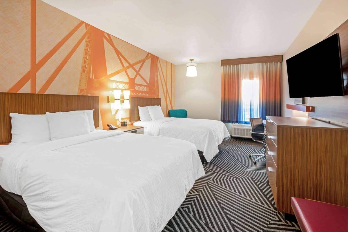 A hotel room with two beds, a desk, a TV, a chair, and a patterned carpet.