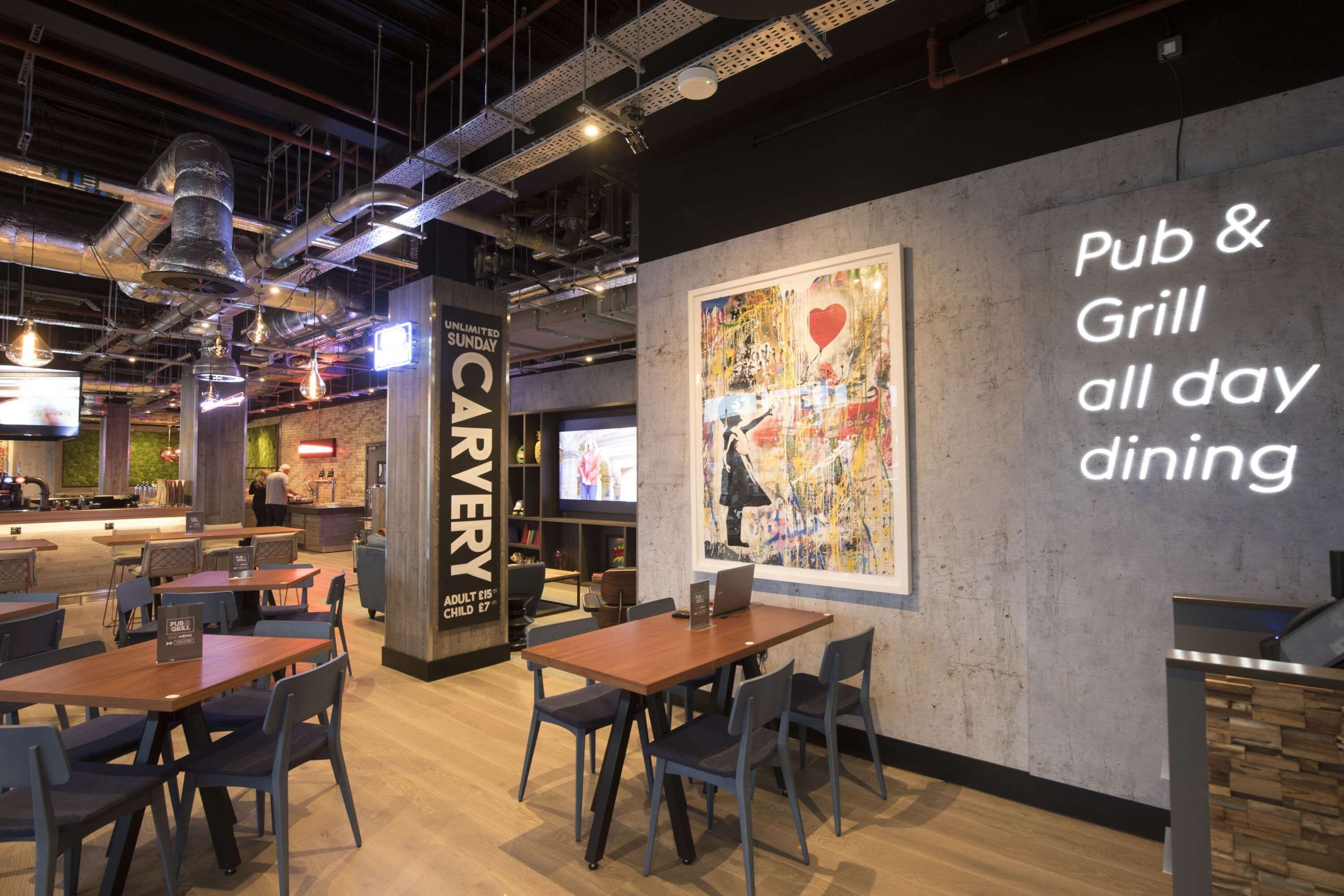 An indoor dining area with tables and chairs, a wall with a 'Pub & Grill all day dining' sign, and a large painting.