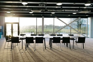 Un salón de conferencias con una larga mesa y sillas, ventanas amplias y vistas a un edificio y árboles.