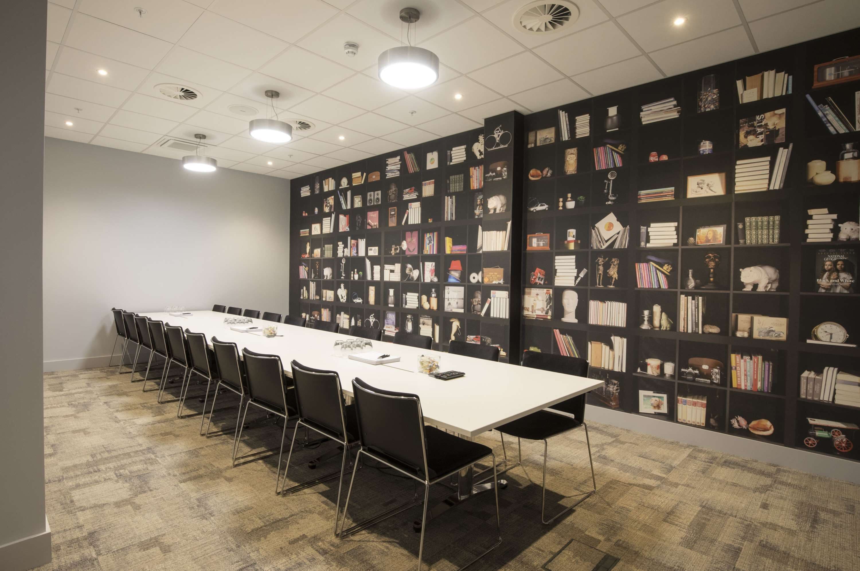 A conference room with a long table, chairs, and a bookshelf wall.