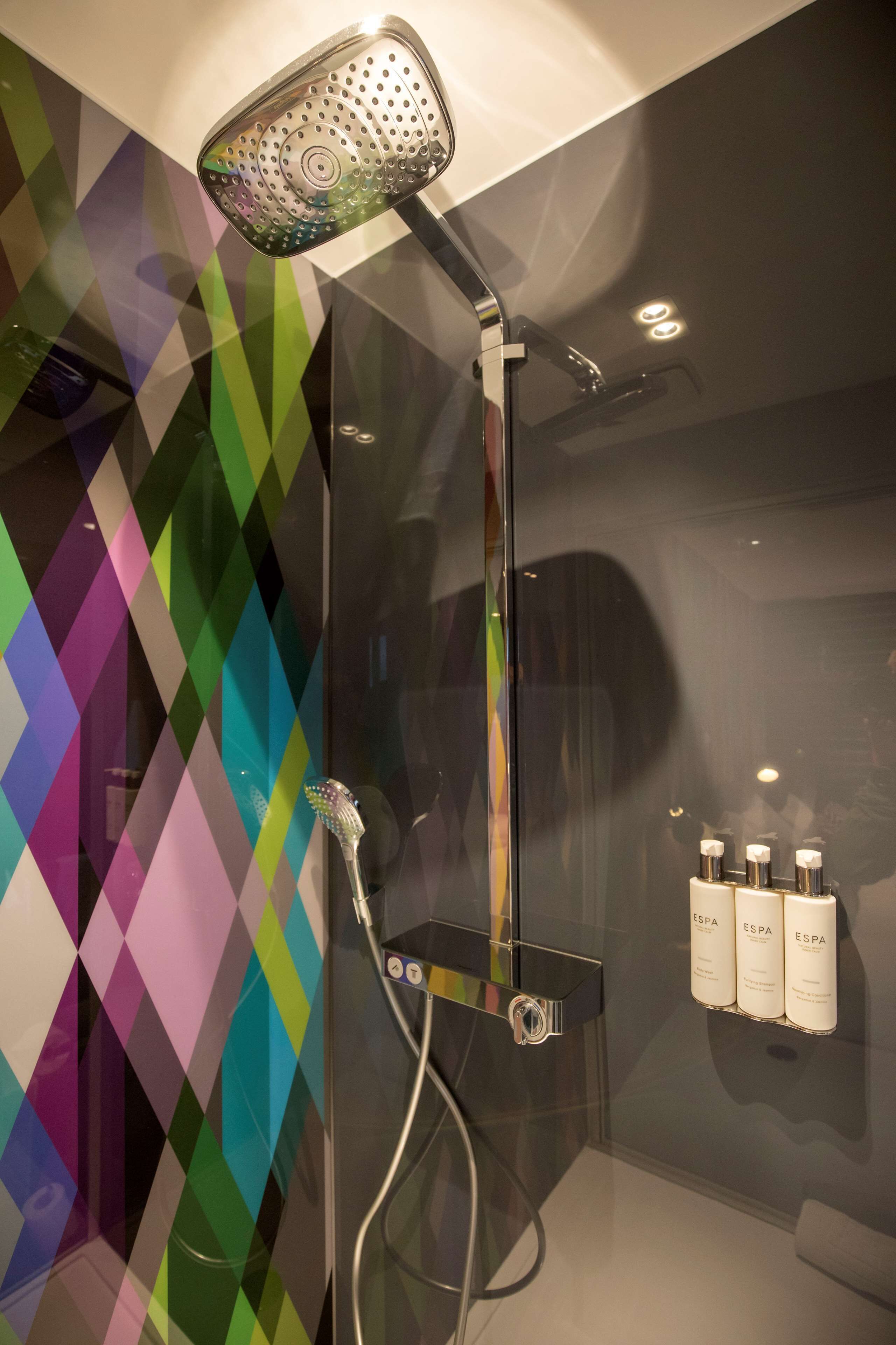 A modern shower with a handheld showerhead, a glass enclosure, and a wall-mounted shelf with toiletries.