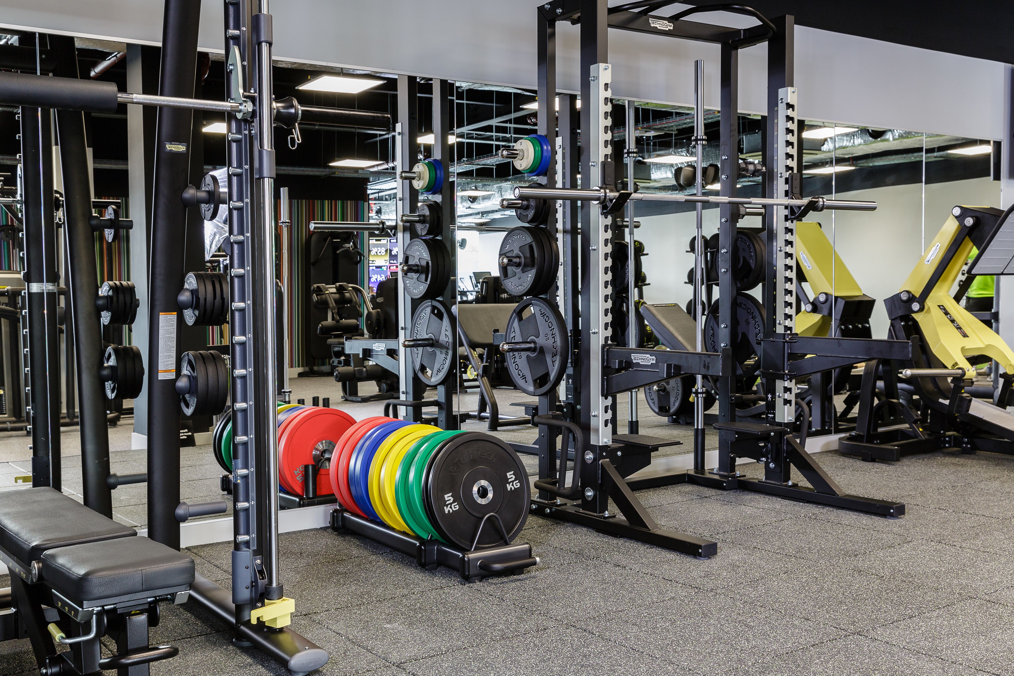 Ein Fitnessraum mit Gewichtebeinrichtungen, darunter Langhanteln und Gewichtsplatten.