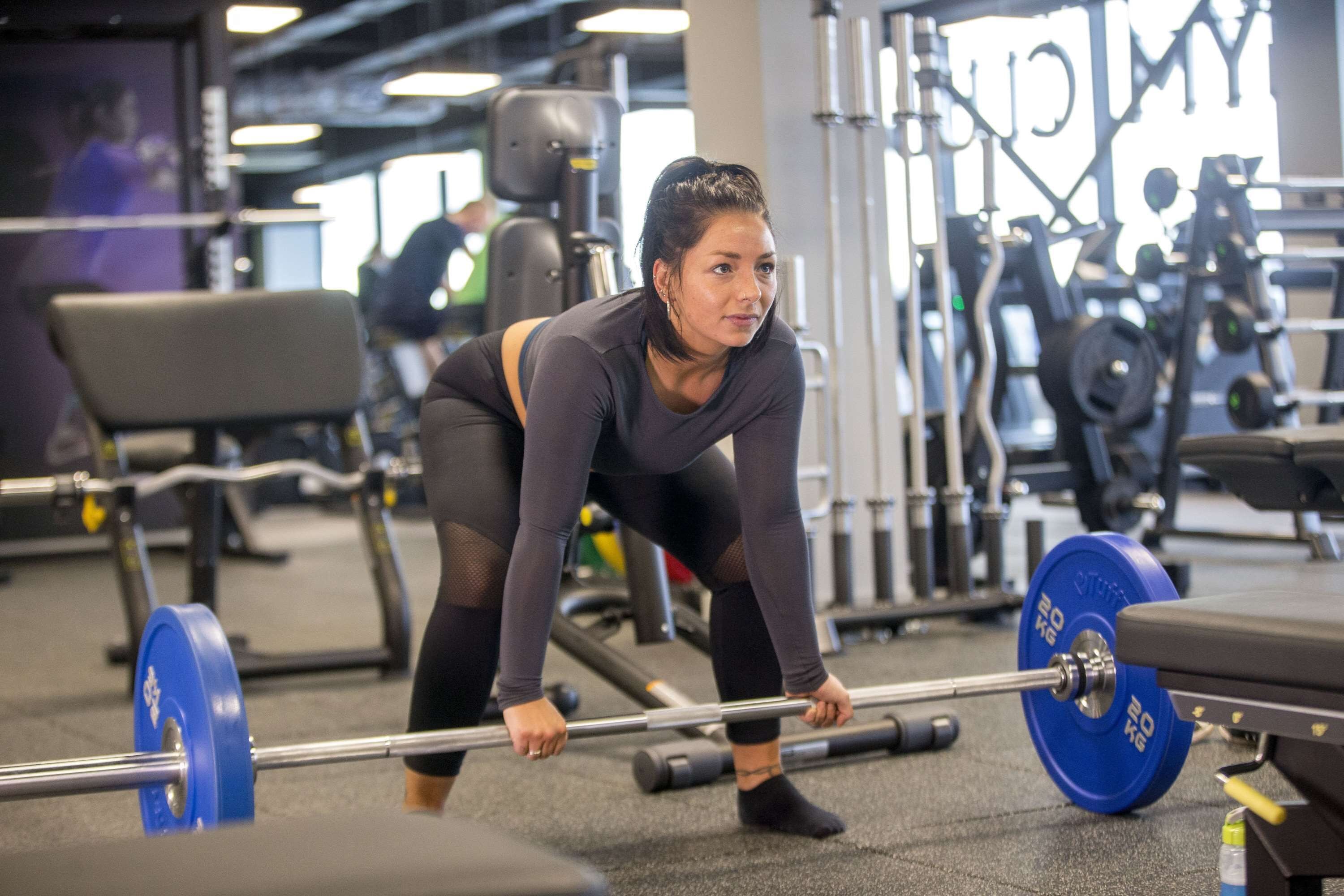 Un gimnasio con equipo de levantamiento de pesas y una persona realizando una sentadilla con barra.