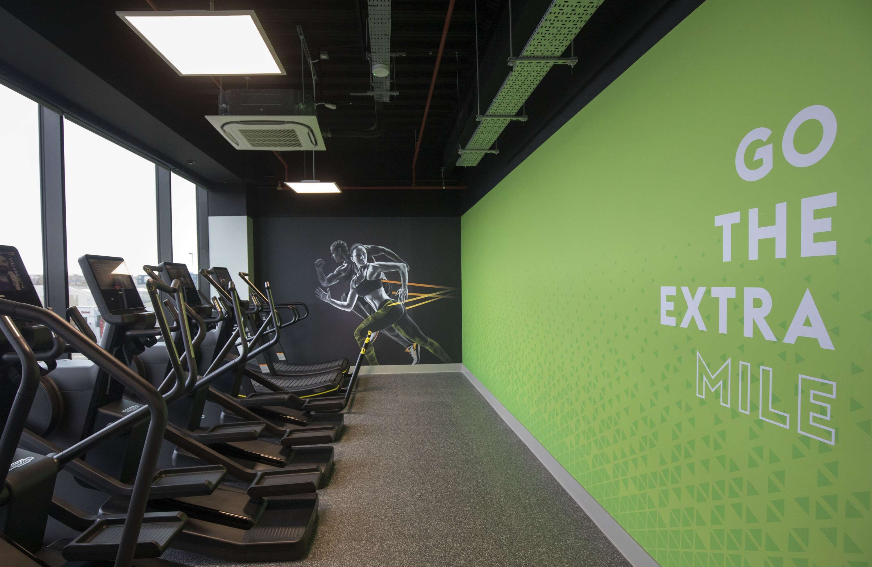 Un gimnasio con cintas de correr, un mural y una pared verde decorativa con texto.