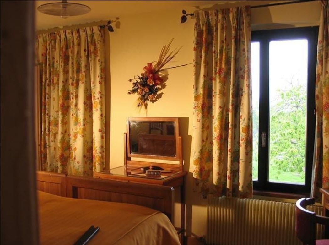 Una habitación con cama, escritorio y radio, y ventana con cortinas.