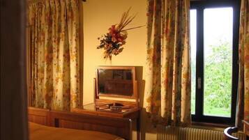 Una habitación con cama, escritorio y radio, y ventana con cortinas.